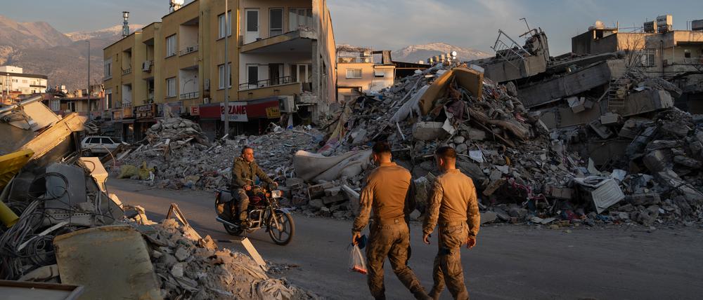 Menschen gehen an den Trümmern zerstörter Gebäude im türkisch-syrischen Grenzgebiet vorbei. 