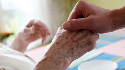 Ein Pfleger hält in einem Pflegeheim die Hand einer Bewohnerin.