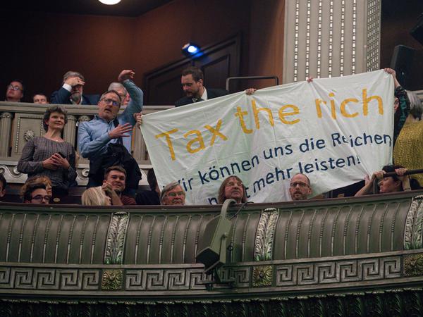 Demonstranten halten beim Dreikönigstreffen der FDP ein Plakat mit der Aufschrift „Tax the rich - Wir können uns die Reichen nicht mehr leisten“ hoch.
