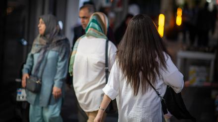 Eine Frau läuft in Teheran mit offenen Haaren am Abend eine Straße entlang, im Hintergrund laufen zwei Frauen mit Kopftuch. (Symbolbild)