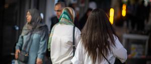 ran, Teheran: Eine Frau läuft in Teheran mit offenen Haaren am Abend eine Straße entlang, im Hintergrund laufen zwei Frauen mit Kopftuch.