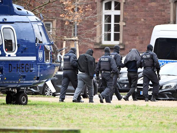 Zwei Personen werden in Karlsruhe von Polizisten bei einem Hubschrauberlandeplatz zu einem Auto geführt. Den Beschuldigten wird die Mitgliedschaft in einer ausländischen terroristischen Vereinigung vorgeworfen. Dazu finden beim Bundesgerichtshof (BGH) Haftprüfungen statt. 