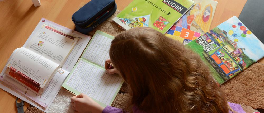 Ein achtjähriges Mädchen liegt auf einem Teppich in ihrem Kinderzimmer und erledigt Hausaufgaben im Fach Deutsch.