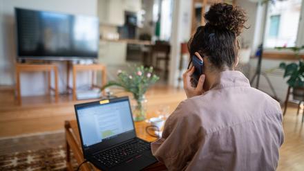 Eine junge Frau, die aufgrund der Corona-Pandemie im Homeoffice arbeitet, nimmt in ihrem Wohnzimmer an einer Telefonkonferenz teil.