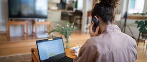 Eine junge Frau, die aufgrund der Corona-Pandemie im Homeoffice arbeitet, nimmt in ihrem Wohnzimmer an einer Telefonkonferenz teil.