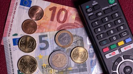Die Summe von 18,94 Euro liegt auf einem Tisch neben der Fernbedienung für einen Fernseher. Der Rundfunkbeitrag soll ab 2025 vorläufigen Berechnungen von Finanzexperten zufolge um 58 Cent steigen. 
