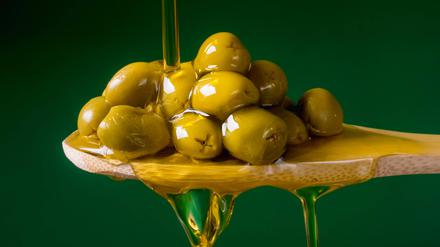 Olivenöl läuft über einen mit Oliven gefüllten Holzlöffel.