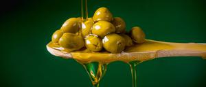 Olivenöl läuft über einen mit Oliven gefüllten Holzlöffel.