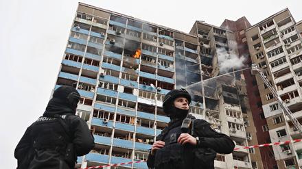 Zwei Sicherheitsbeamte stehen vor einem brennenden Hochhaus in Kiew, das von russischen Luftangriffen getroffen wurde.