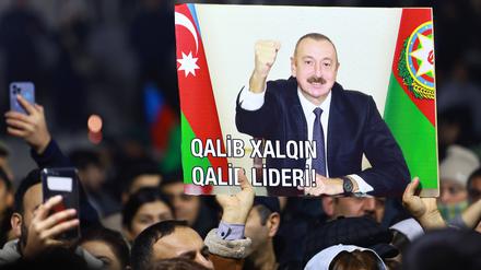 Menschen in Baku (Aserbaidschan) halten ein Plakat des Präsidenten in die Höhe.