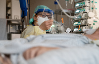 Ein Facharzt versorgt einen Covid-19-Patienten auf der Intensivstation der Leipziger Uniklinik und hält dessen Hand. Foto: dpa/Jan Woitas