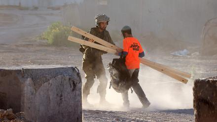 Ein israelischer Soldat fängt einen rechten Aktivisten ab, der Holz für den Bau eines Gebäudes in der Militärzone zwischen dem Zaun und der Mauer, die Israel vom Gazastreifen trennt, trägt. 
