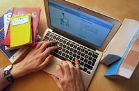 Ein junger Mann ruft zwischen Schul- und Lehrbüchern auf einem Laptop die Internetseite von Facebook auf. Foto: Karl-Josef Hildenbrand/dpa