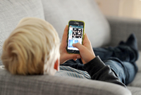 Ein Kind liegt auf einem Sofa und blickt auf sein Smartphone. Foto: Tobias Hase / dpa