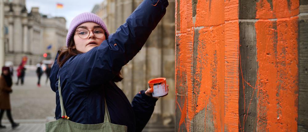 16.11.2023, Berlin: Eine Klimaaktivistin bemalt das Brandenburger Tor mit oranger Farbe. Die Gruppe Letzte Generation teilte am Donnerstag mit, dass Mitglieder mit Pinseln die Westseite des Bauwerks eingefärbt haben. Die Polizei Berlin berichtete, dass zwei Klimaaktivisten festgenommen wurden. Foto: Annette Riedl/dpa +++ dpa-Bildfunk +++