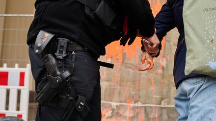 Ein Polizeibeamter (l) nimmt eine Klimaaktivistin in Gewahrsam, die das Brandenburger Tor mit oranger Farbe bemalt hat. 