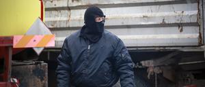 Ein maskierter Mann aus Serbien sieht zu, wie Lastwagen von der Rudare-Barrikade entfernt werden.