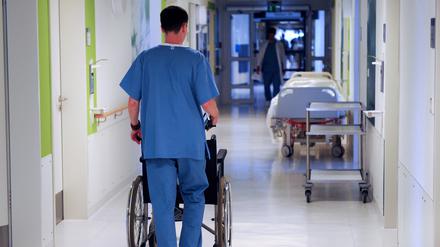 Ein Pfleger schiebt einen Rollstuhl über einen Flur in einem Krankenhaus. 