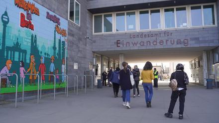 Menschen gehen am Landesamt für Einwanderung  am Friedrich-Krause-Ufer neben einem Wandbild entlang. 