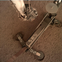 Foto des Marsmaulwurfs, aufgenommen von einer Kamera am Roboterarm der NASA-Sonde "Insight". An den Standfüßen sieht man, wie sich das Gehäuse durch das Hämmern verschoben hat. Die Rammsonde selbst ist rechts oben. Foto: NASA/JPL-Caltech