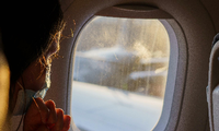 Eine Fluggästin mit Maske schaut vor dem Start aus dem Fenster. Foto: Andreas Arnold/dpa