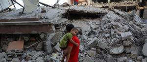 Ein Mann geht mit einem Kind auf dem Arm an einem durch israelische Luftangriffe zerstörten Gebäude in der Stadt Chan Junis im südlichen Gazastreifen vorbei.