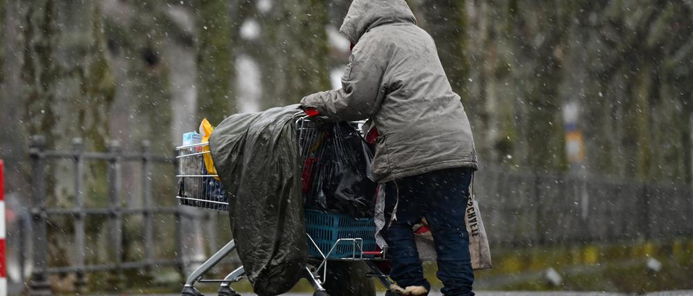 Ein Mensch ohne Obdach transportiert seine Habseligkeiten in einem Einkaufswagen.