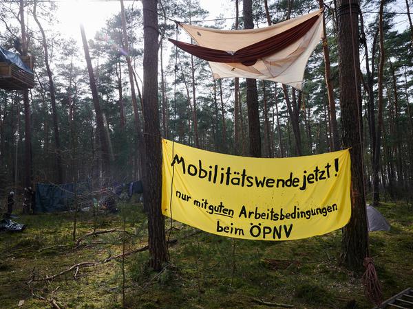 „Mobilitätswende jetzt! Nur mit guten Arbeitsbedingungen bem ÖPNV“ steht auf einem Banner im Wald bei einer Protestaktion gegen die Erweiterung der Tesla-Autofabrik. 