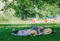 Zwei Menschen liegen mit Strohhut über dem Gesicht im Schatten eines Baumes im Tiergarten. Foto: picture alliance/dpa