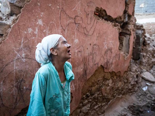 Eine Frau in Marrakesch steht verzweifelt vor den Trümmern ihres Hauses.