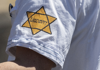 "Ungeimpft" steht auf einem nachgebildeten "Judenstern" am Arm eines Mannes auf einer Demonstration. Foto: Boris Roessler/dpa