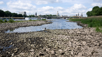Ein trockengefallenes Flussufer mit Altstadt im Hintergrund. Foto: Christian Knieps/dpa