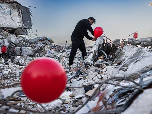 Nach dem Erdbeben in der Türkei hängt ein Mann im Februar in Antakya rote Ballons an die Trümmer. Es sollen die „letzten Spielzeuge“ der Kinder sein, die beim Erdbeben im Februar 2023 umgekommen waren.