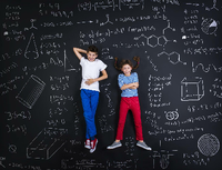 Ein Junge und ein Mädchen liegen lachend auf einer schwarzen Tafel, die mit mathematischen Formeln und Formen vollgeschrieben ist. Foto: Getty Images/iStockphoto