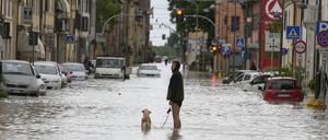 Ein Mann geht mit seinem Hund auf einer überschwemmten Straße spazieren. 