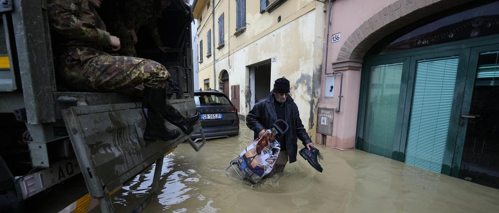 17.05.2023, Italien, Castel Bolognese: Ein Anwohner geht an einem Armeelastwagen in einem überschwemmten Dorf vorbei.