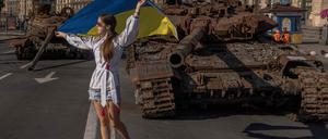 Eine Frau posiert mit ukrainischer Flagge vor einem zerstörten russischen Panzer.