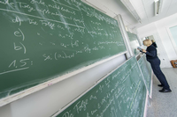 Eine Dozentin schreibt mathematische Formeln an die Tafel. Foto: imago/Agentur 54 Grad