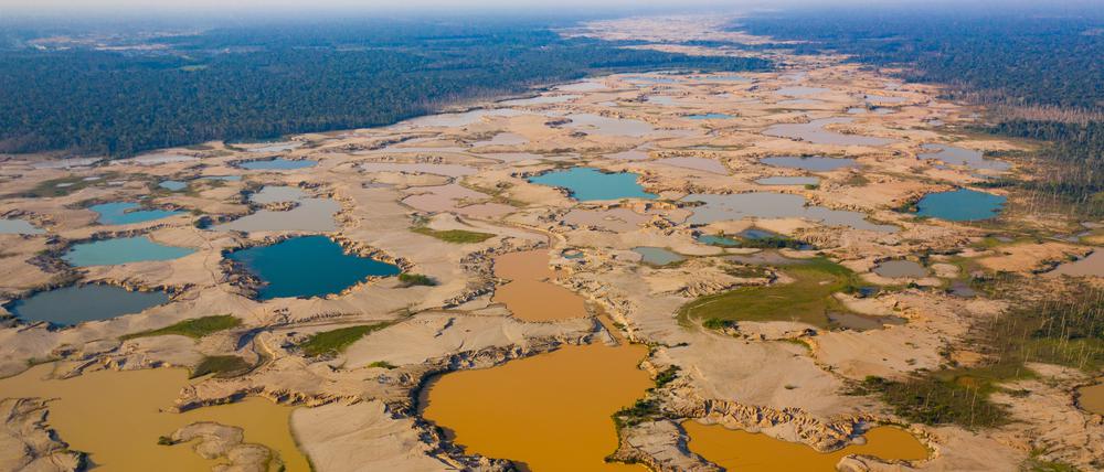 Flache Bergwerksteiche überschwemmen ein ehemaliges Flusssystem in der Region La Pampa in Madre de Dios, Peru. Die Farben der Teiche spiegeln Schwebstoffe und Algenwachstum nach der Einstellung des Goldabbaus wider.