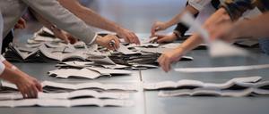 Wahlhelfer und Wahlhelferinnen zählen in einem Wahllokal Stimmzettel für die Bundestagswahl. 