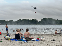 Bizzare Szenerie. Badegäste hocken am Strand des Seddiner Sees, während ein Löschhubschrauber der Bundeswehr Wasser schöpft. Foto: dpa/Stephanie Pilick