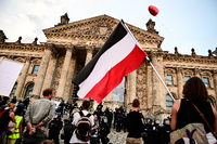 Teilnehmer einer Kundgebung gegen die Corona-Maßnahmen stehen vor dem Reichstagsgebäude - mit Reichsflagge. Foto: picture alliance/dpa