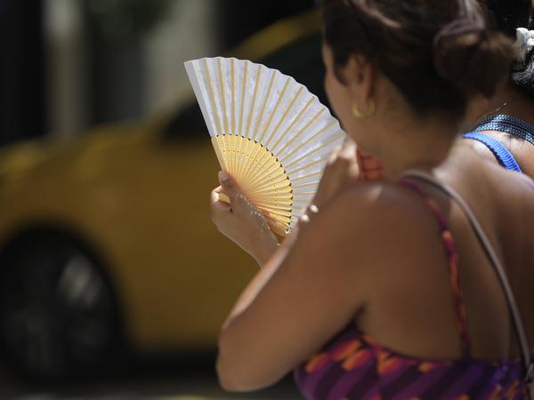 Eine Frau spaziert bei großer Hitze mit einem Fächer durch die Innenstadt von Palma. 