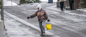 Eine Frau verteilt Streusalz bei Regen und Schneeglätte auf einem Fußweg in Heilbronn.