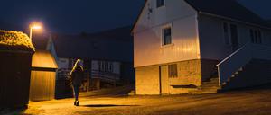 Eine Frau läuft nachts in einer Straße eines kleinen Dorfes entlang.