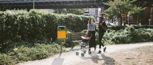 Young man carrying daughter on shoulders while woman pushing baby stroller at footpath against railway bridge