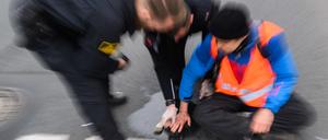 Polizisten versuchen festgeklebte Hände von Aktivisten der Gruppierung «Letzte Generation» am Deisterkreisel in Hannover mit Speiseöl von der Straße abzulösen. 