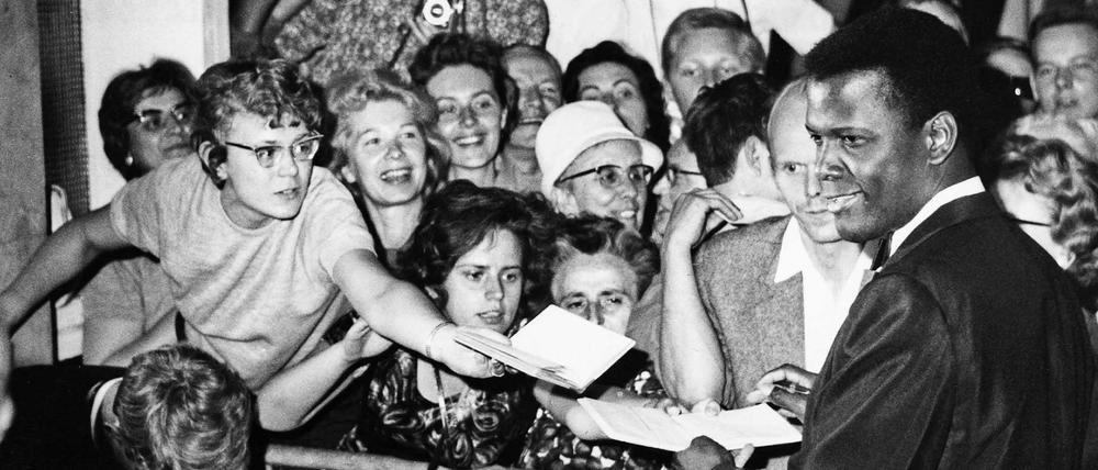 Sydney Poitier auf der Berlinale 1964, umringt von Fans, die zur besseren Sicht die Baukastenfassade der Kongresshalle hochklettern.