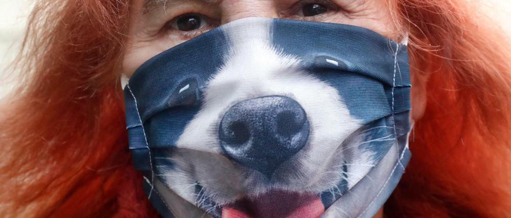 Eine Frau in den USA trägt während eines Spaziergangs eine Stoffmaske, auf der ein Bild einer Hundeschnauze gedruckt ist.