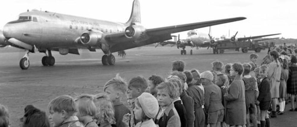 Kinder stehen auf dem Flughafen Berlin-Tempelhof und sehen der Landung eines US-amerikanischen Transportflugzeuges zu.